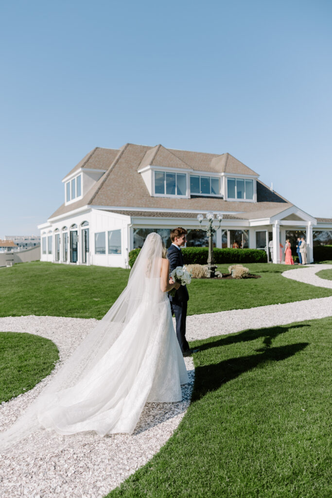 Groom and bride walk at wedding with Belle Mer wedding venue in background