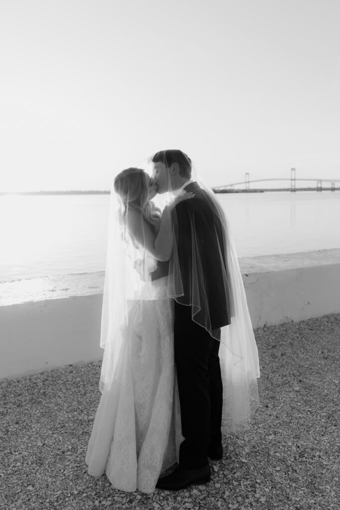 Black and white photo of bride and groom kissing with veil over them