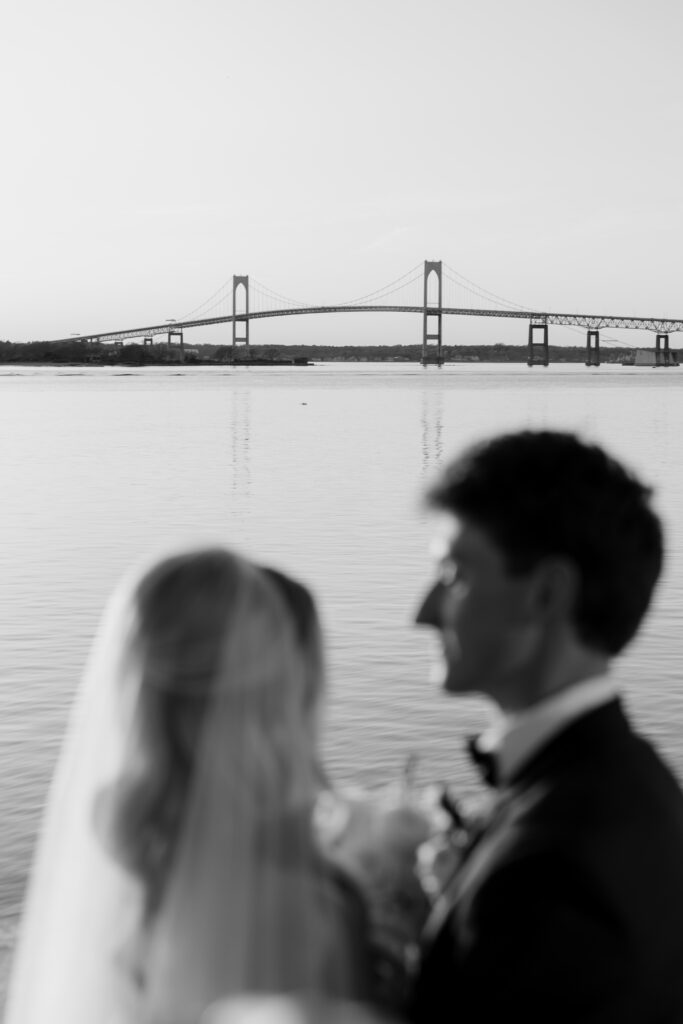 Black and white photo of the Claiborne Pell Newport Bridge with bride and groom blurred in the front