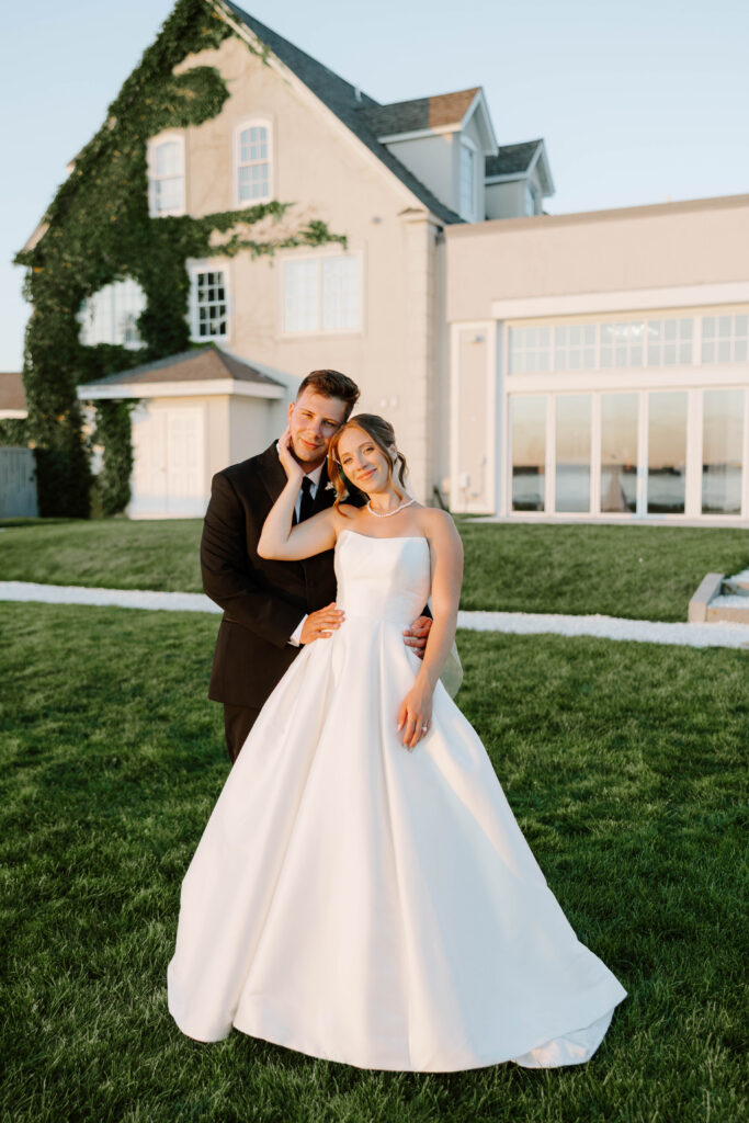 Sunset portrait of bride holding grooms cheek with Belle Mer wedding venue in the background