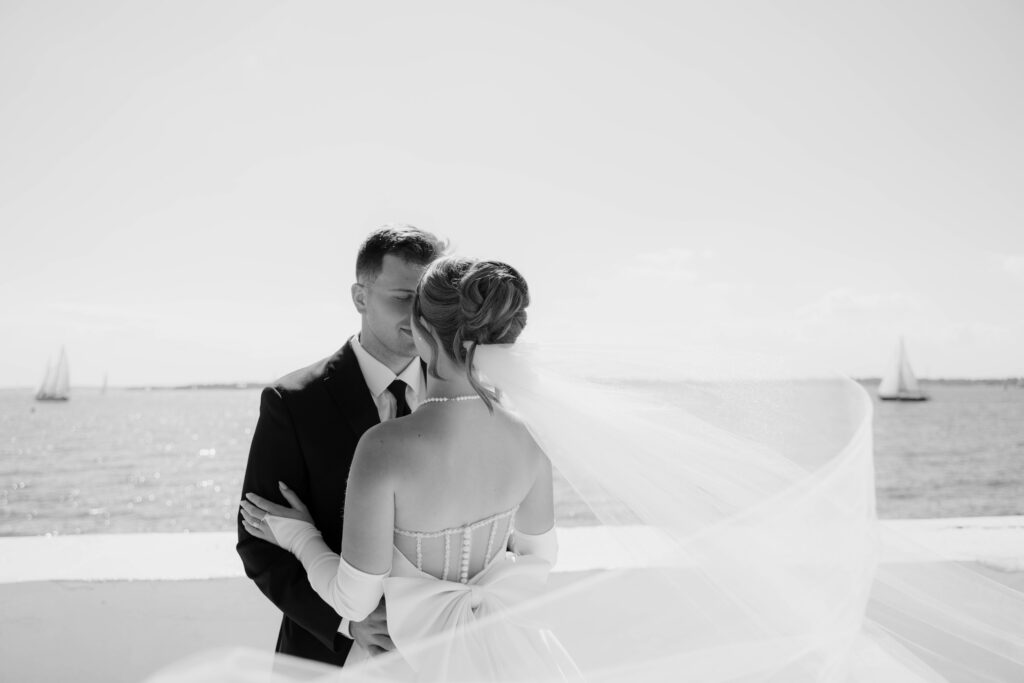 Black and white photo of bride and groom looking at each other with veil flowing in the wind