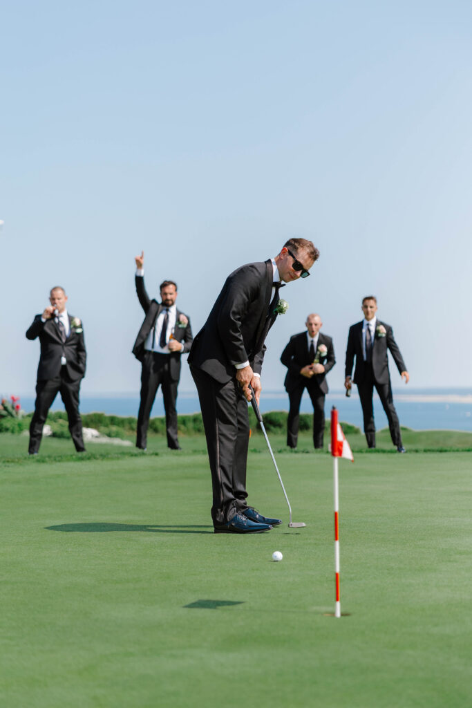 groomsmen photo on golf course with men cheering behind as groom puts into hole