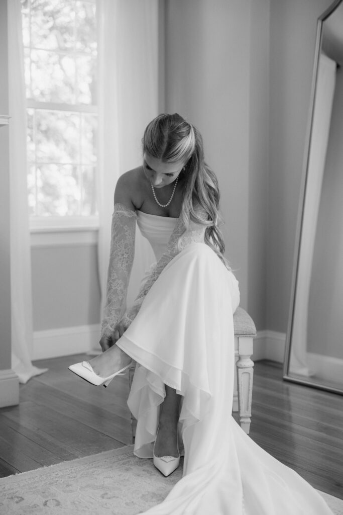 Black and white photo of bride putting shoes on on wedding day