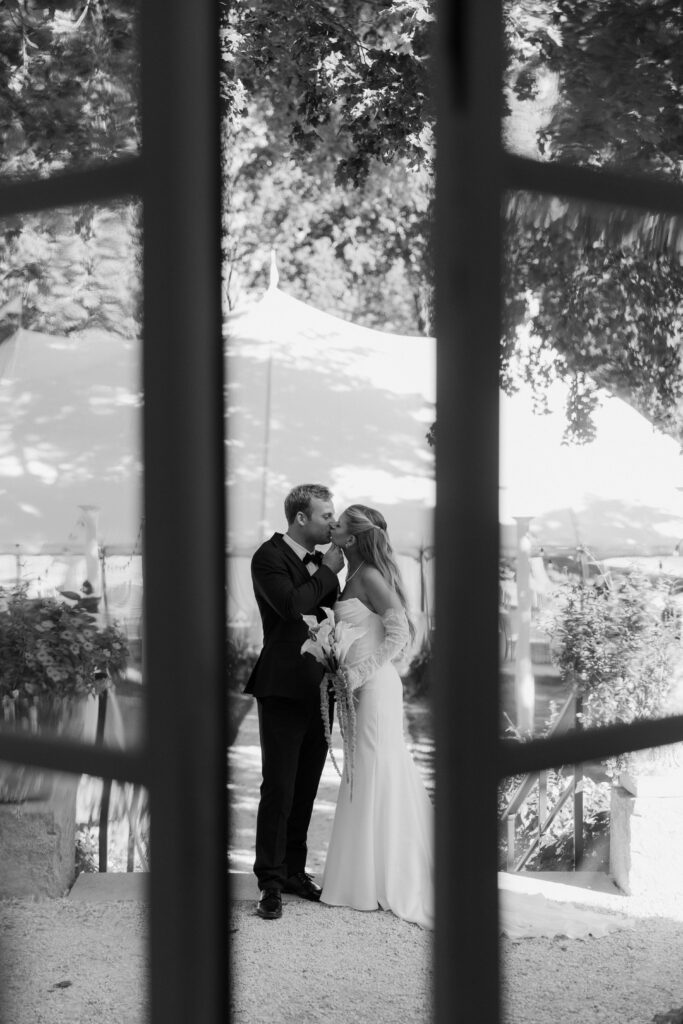 Black and white photo of bride and groom kissing with tent in the background