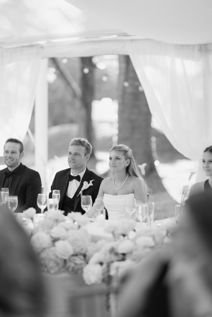 Black and white photo of bride and groom listening to toast at wedding reception
