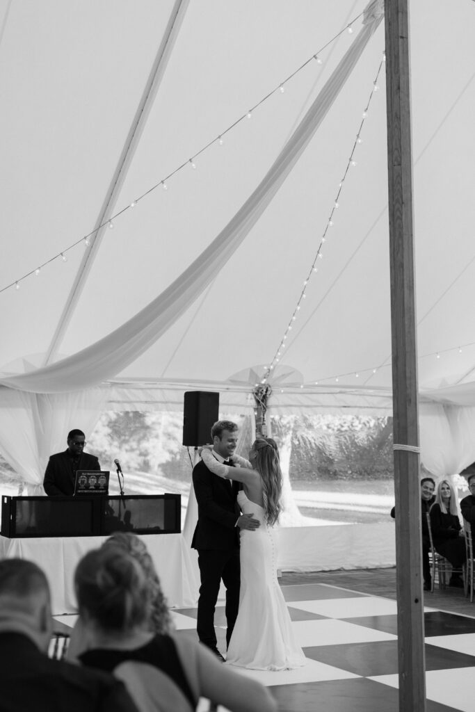Black and white photo of bride and groom sharing first dance in tented reception