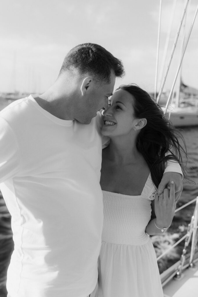 Black and white photo of man and woman touching noses with ocean in background