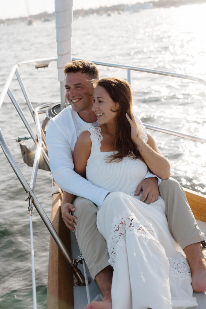 Man and woman sit and hug on sailboat during their engagement session