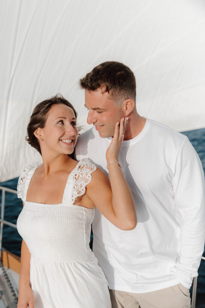 Man and woman look at each other on sailboat during engagement session
