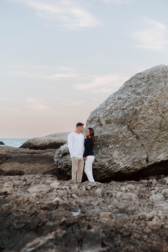 Man and woman look at each other on rocky coast in New England