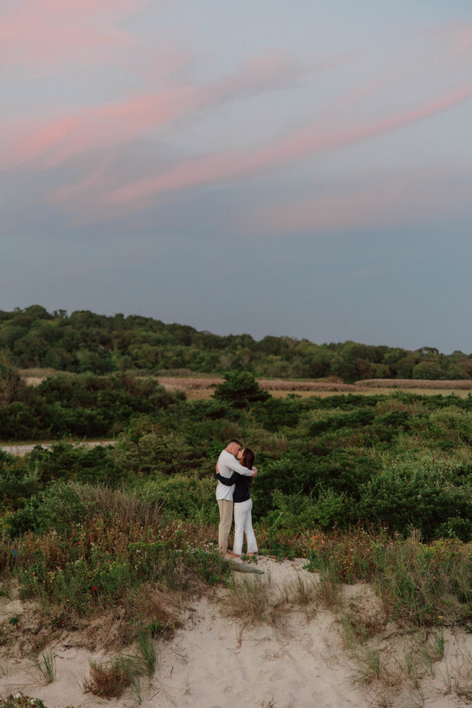 Wide photo of man and woman hugging on sand dunes with beautiful sunset in the background